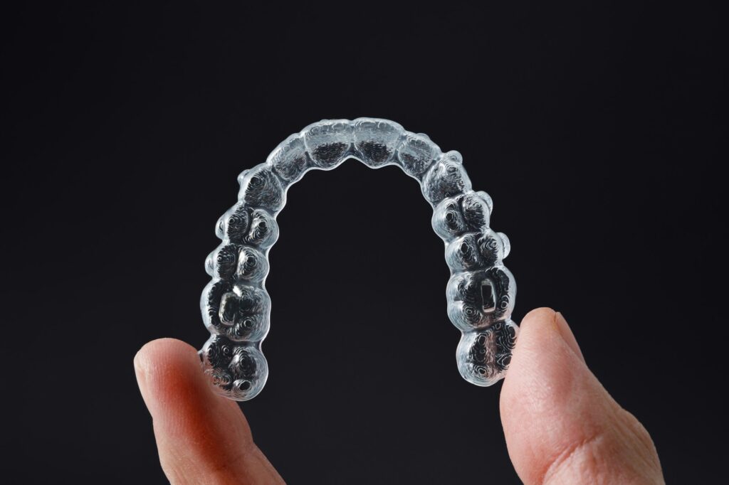 Hand holding one transparent retainer on black background. Invisalign orthodontics concept