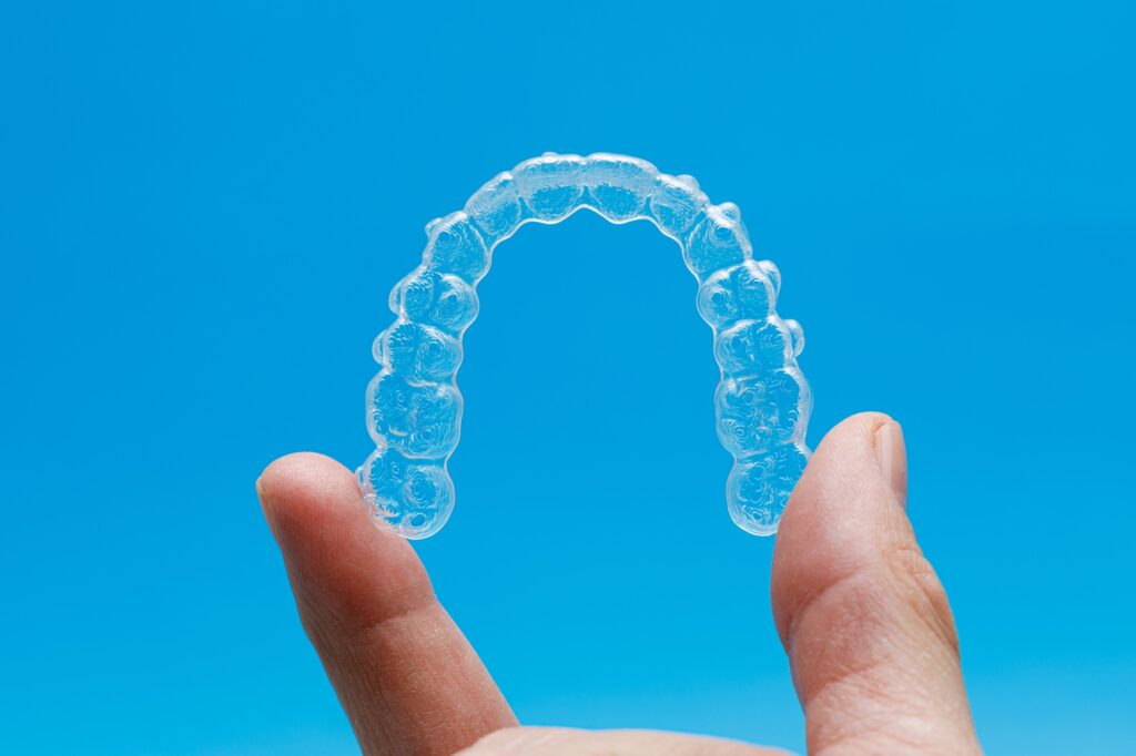 Hand holding one transparent retainer on blue background. Invisalign orthodontics concept